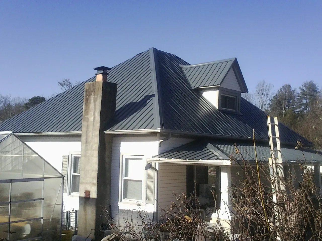 Dark blue standing seam metal roof on a white farmhouse with dormer — Slate & Tile Roof Repair by Roofing Brothers in Lake Como