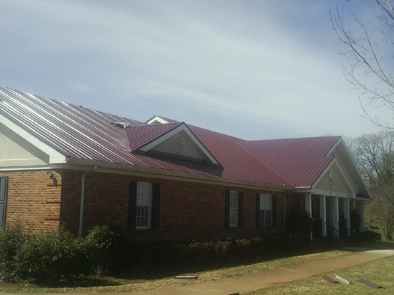 Red metal roof with gabled entries on a long brick building, from a Hail Damage Roof Repair job in Lake Como