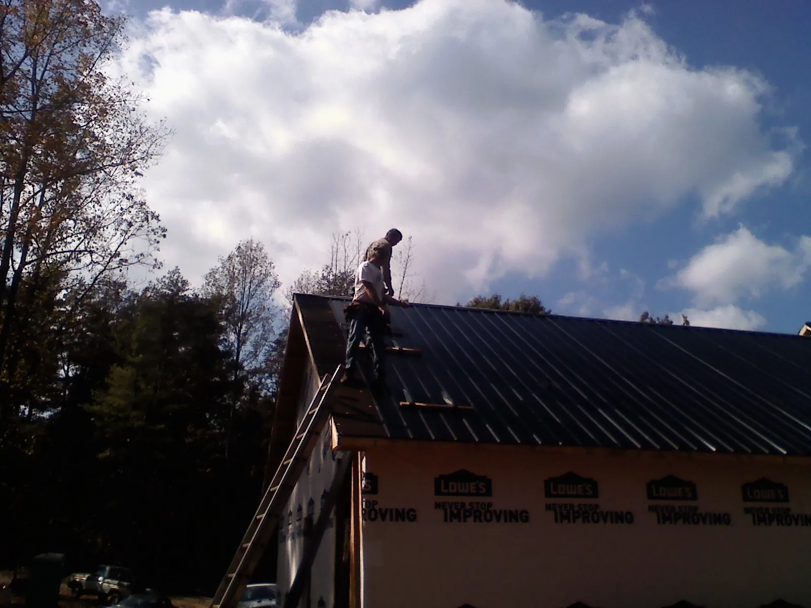 Roofer fastening dark metal panels high against a cloudy sky, from a Roof Inspection job in Lake Como