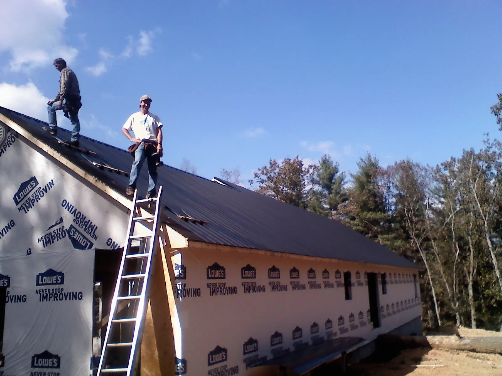 Two roofers standing on a long dark metal roof over a wrapped building in Lake Como
