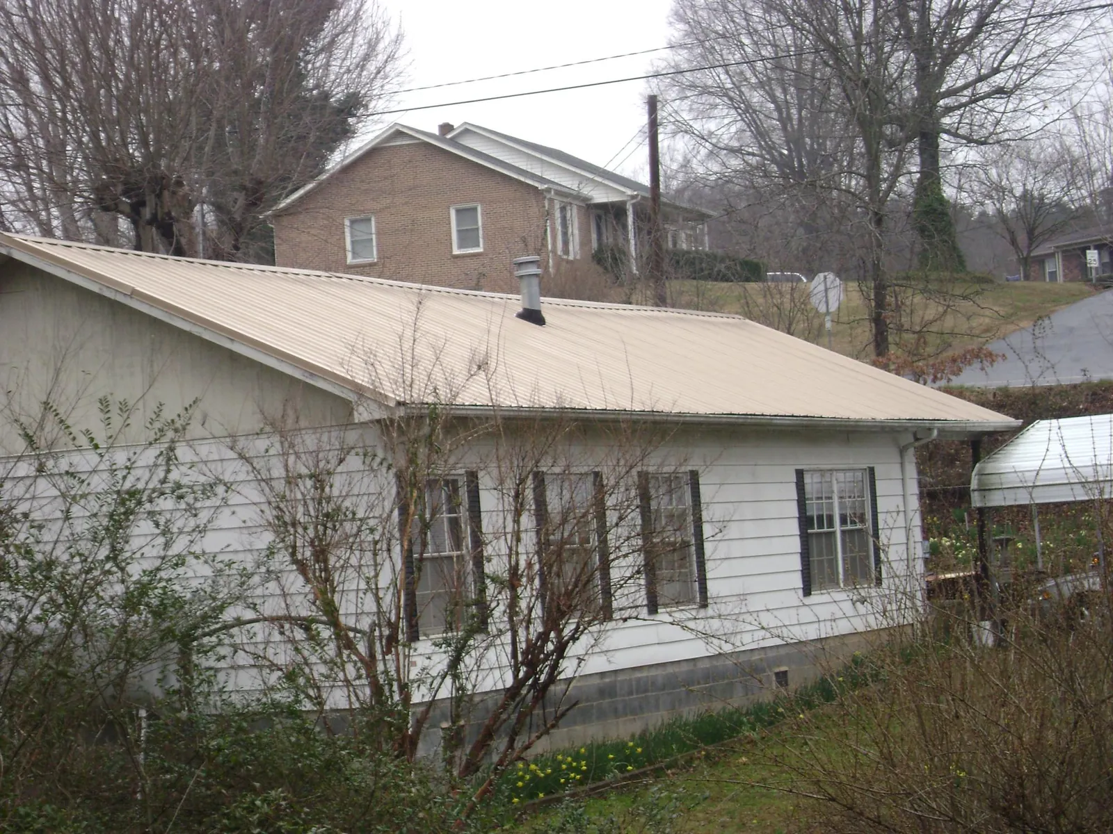 Tan metal roof on a white sided house set into a hillside — Commercial Roofing by Roofing Brothers in Lake Como