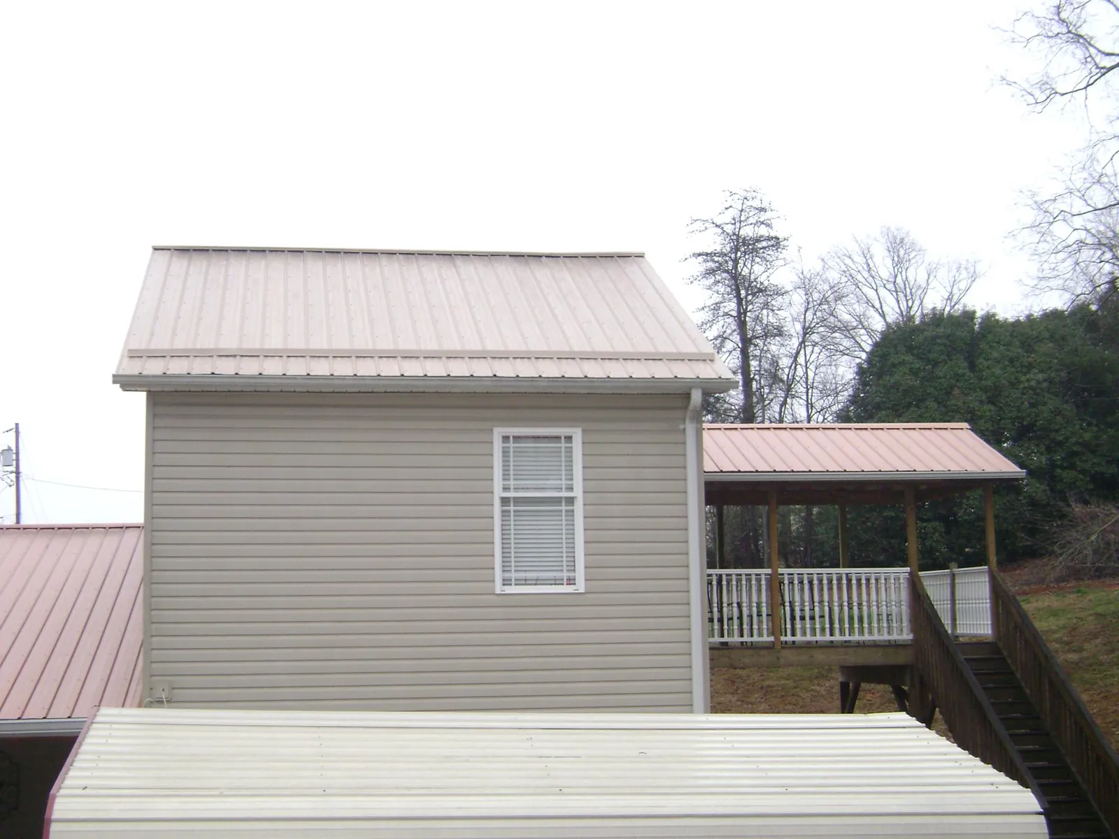 Tan metal roofs on a two story addition and attached porch, from a Roof Replacement job in Lake Como
